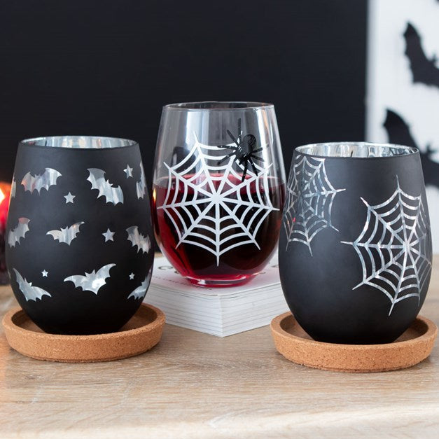 Halloween-themed tumblers with spider webs, bats, and a spider on a wooden surface.