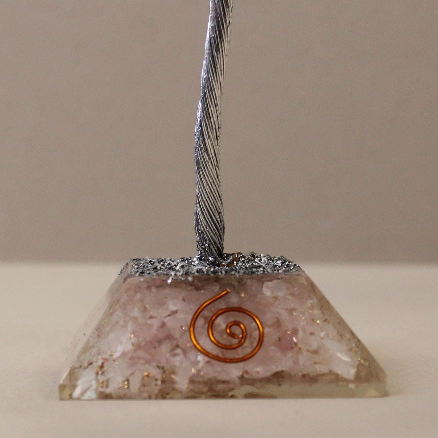 Pyramid-shaped object with metallic top and spiral design on a beige background