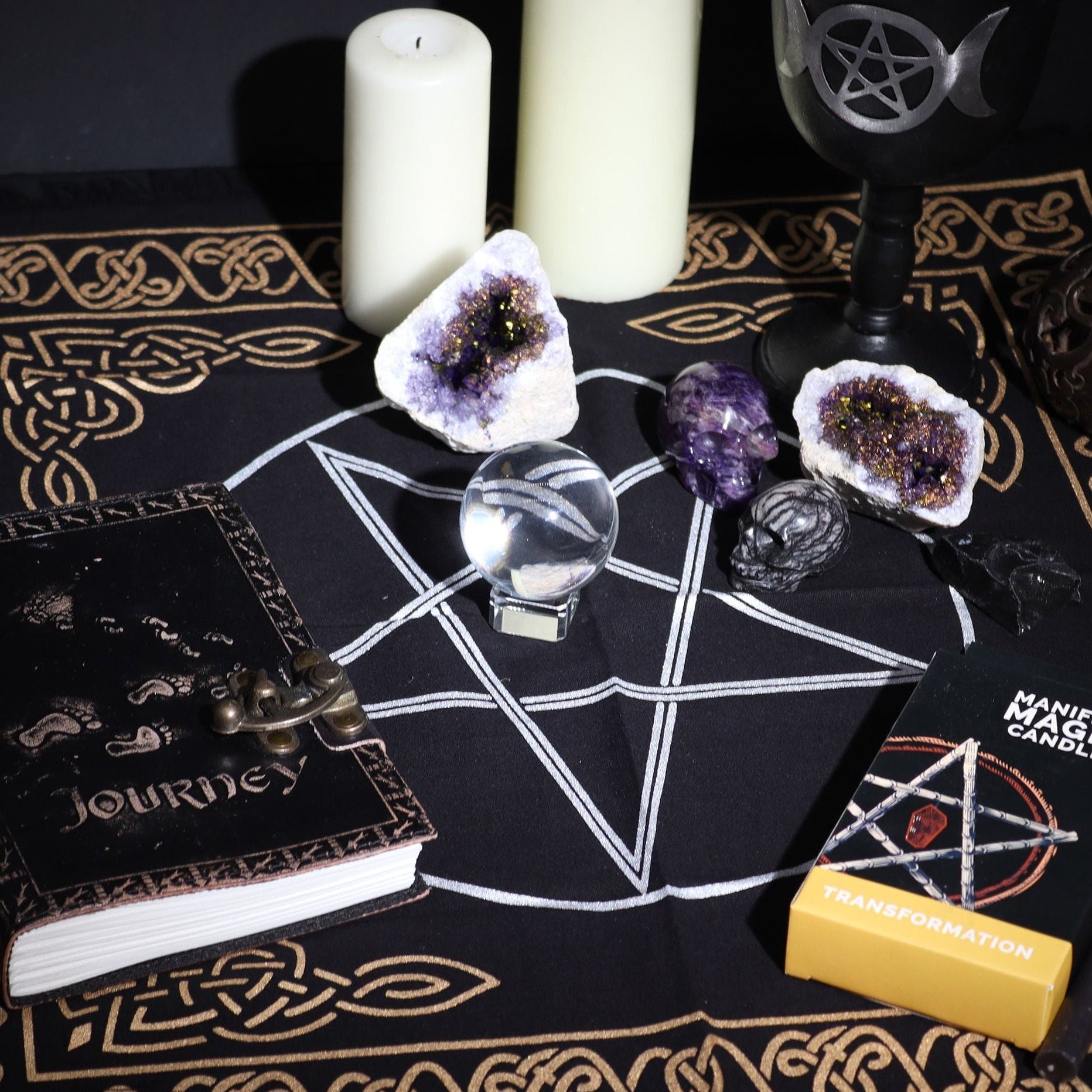 Witchcraft altar setup with candles, crystals, and books on a black cloth with white designs.