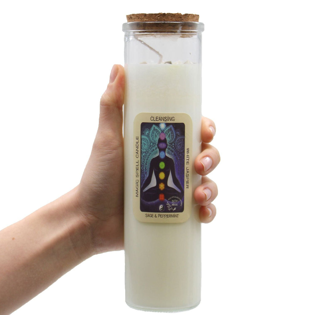 Hand holding a white candle in a glass jar with a label on a white background