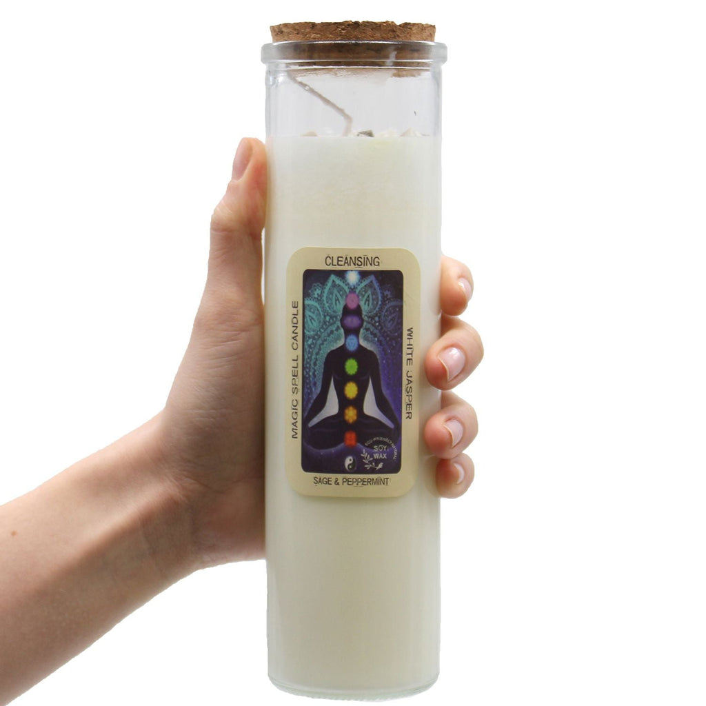 Hand holding a white candle in a glass jar with a label on a white background