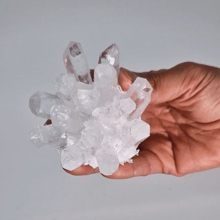 Clear crystal cluster held in a hand against a light gray background