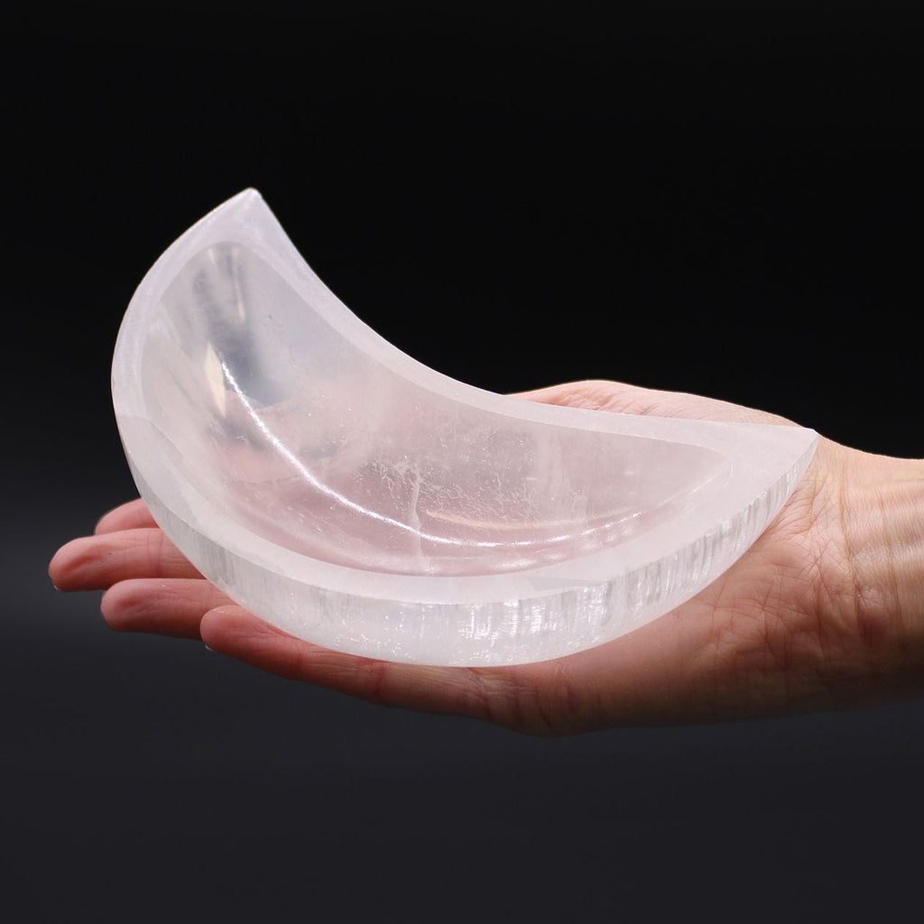 Clear silicone mold shaped like a crescent moon held in a hand against a black background