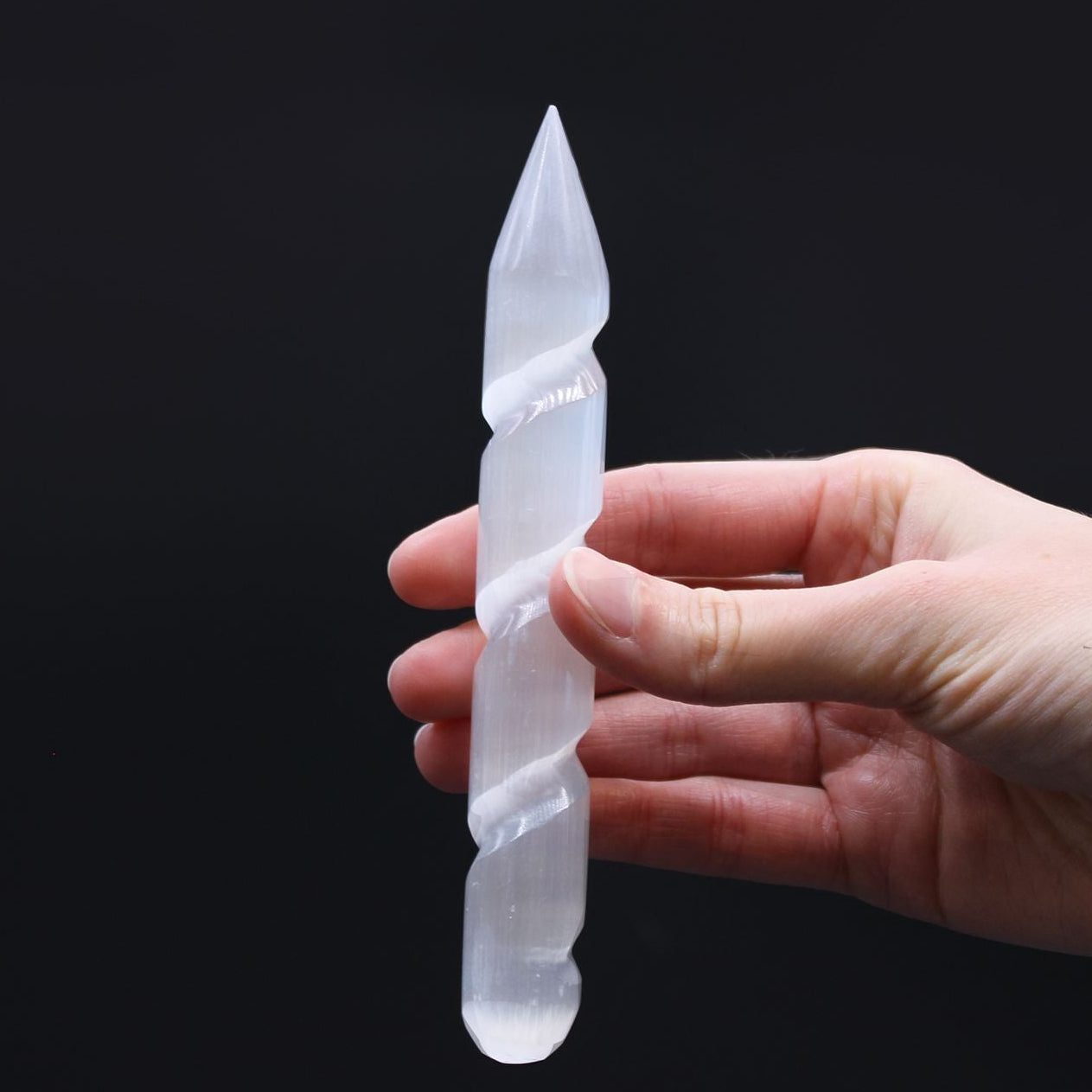 Hand holding a clear crystal object against a black background