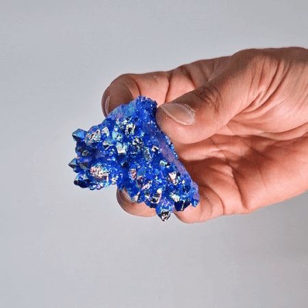 Hand holding a blue crystal cluster against a plain background