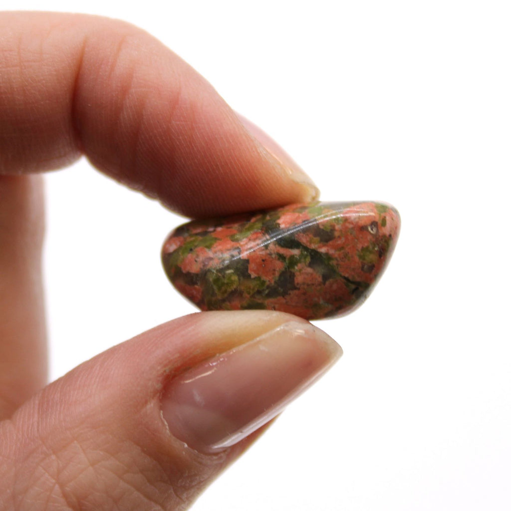 Hand holding a multicolored stone against a white background