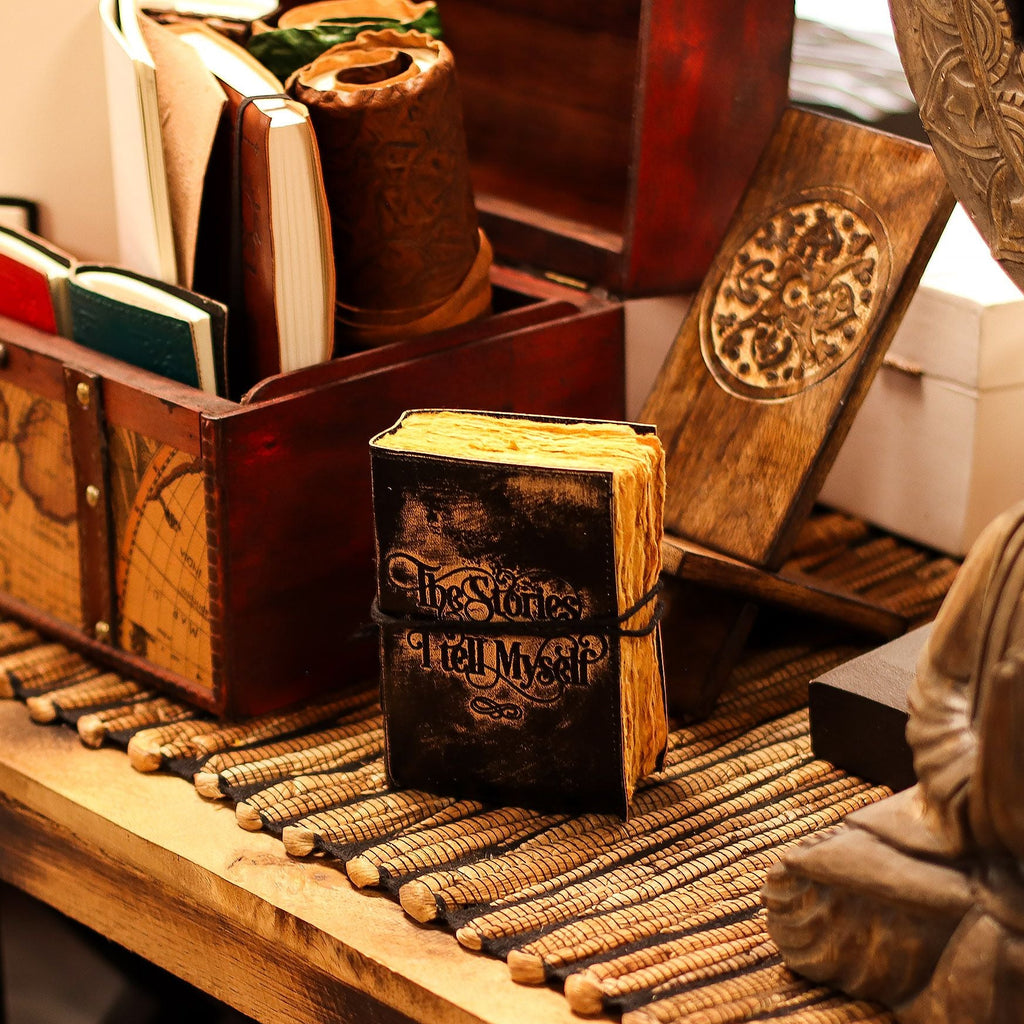 Decorative book with 'The Stories Tell Themselves' text on a wooden surface with a statue and books in the background.
