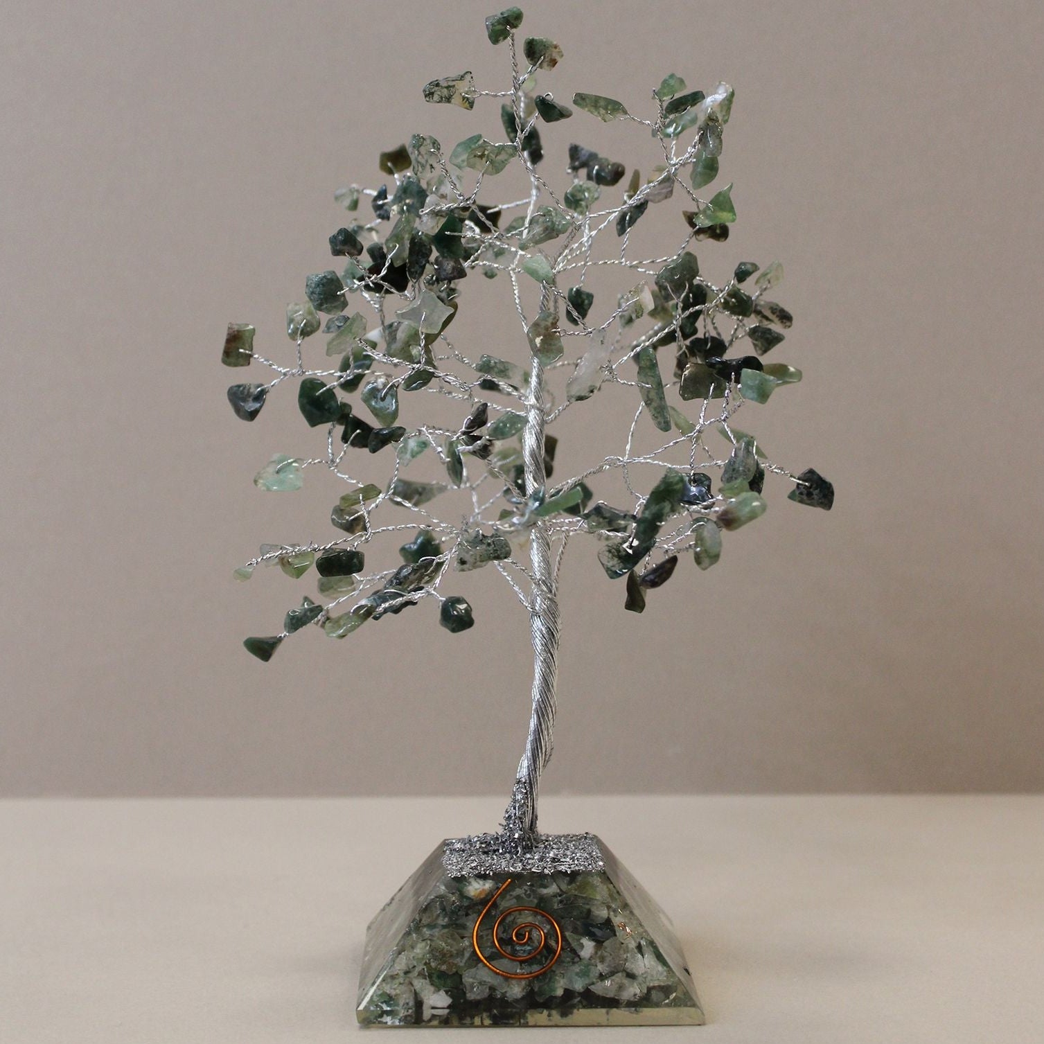 Decorative tree sculpture with green leaves and a metallic base on a plain background
