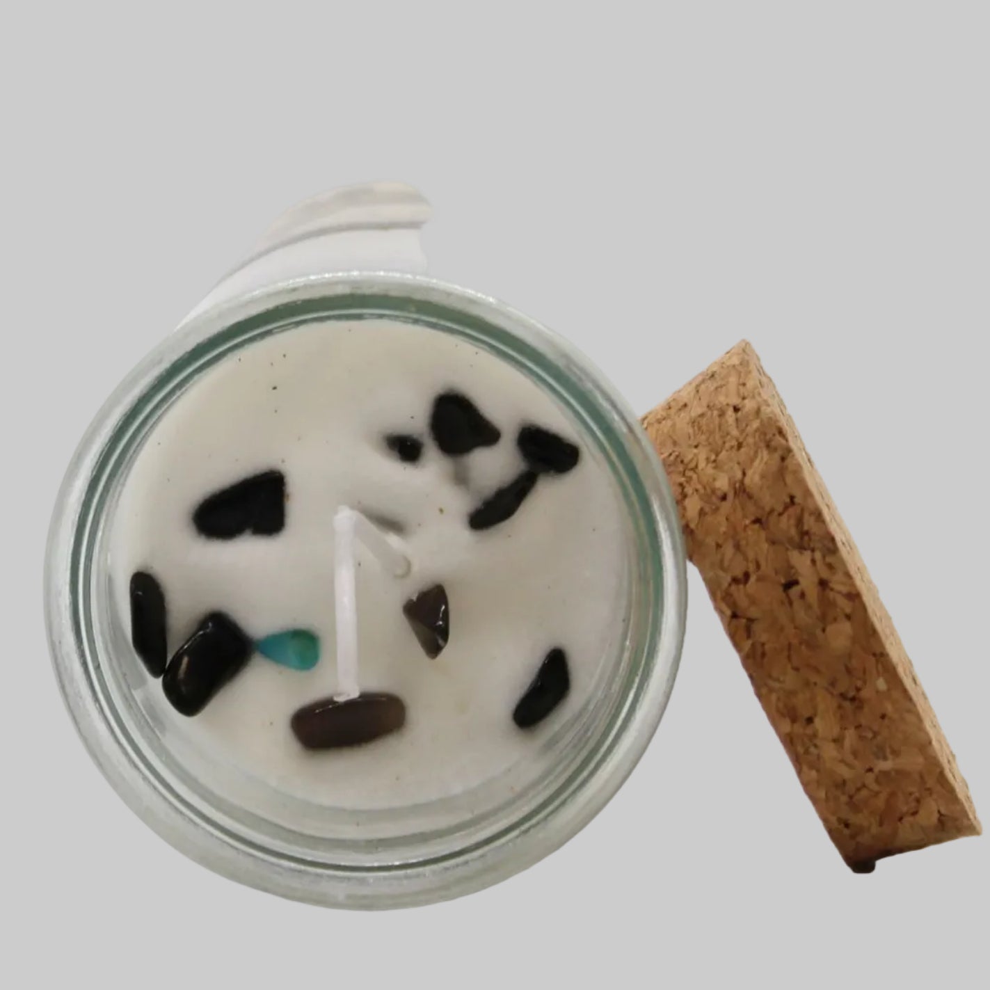 Candle in a glass jar with decorative stones and a cork lid on a white background