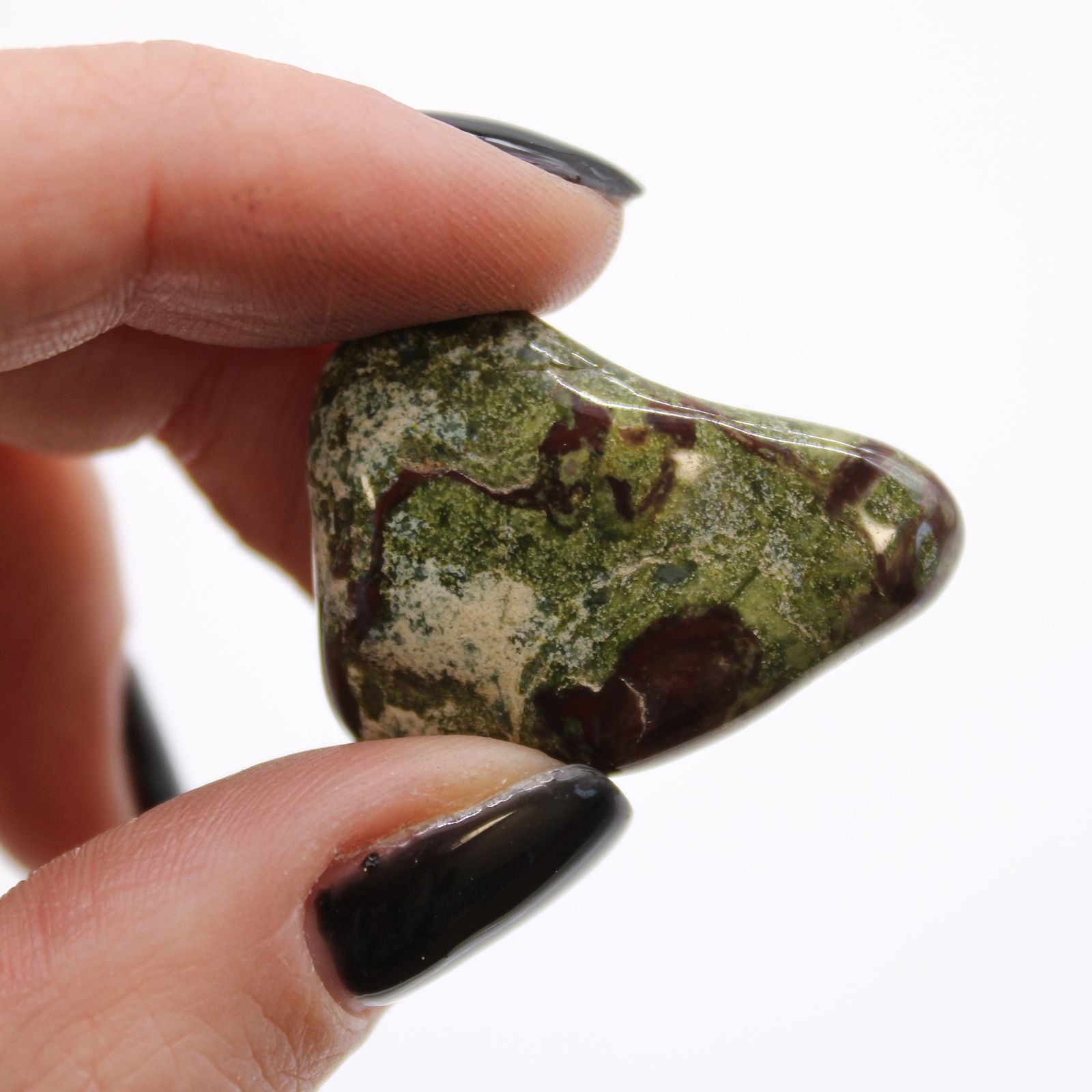Hand holding a green and brown stone against a white background