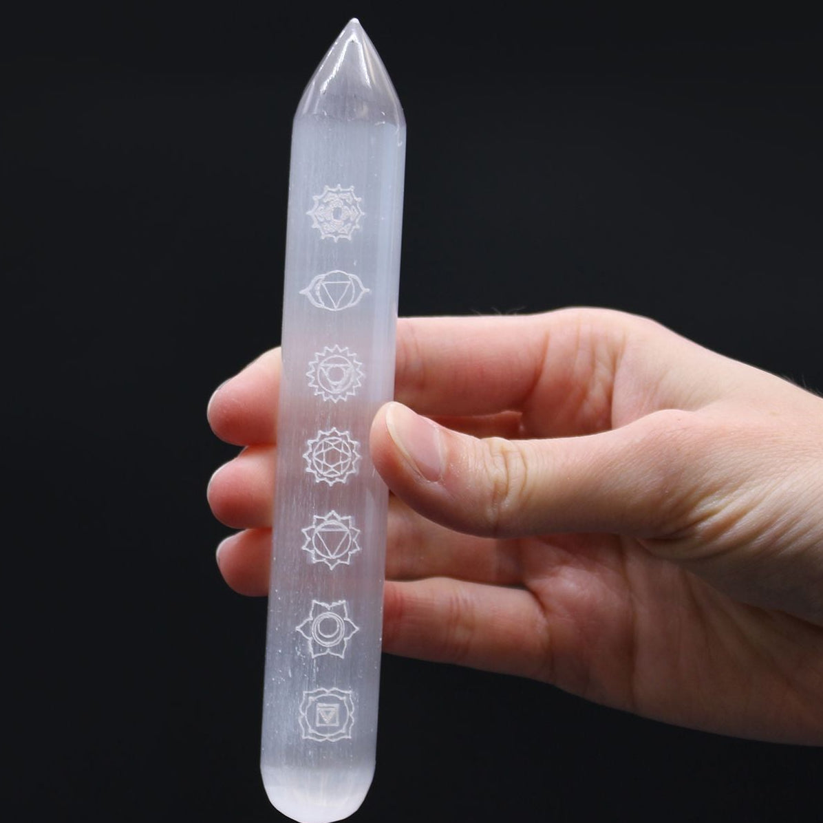 Crystal wand with engraved symbols held in a hand against a black background