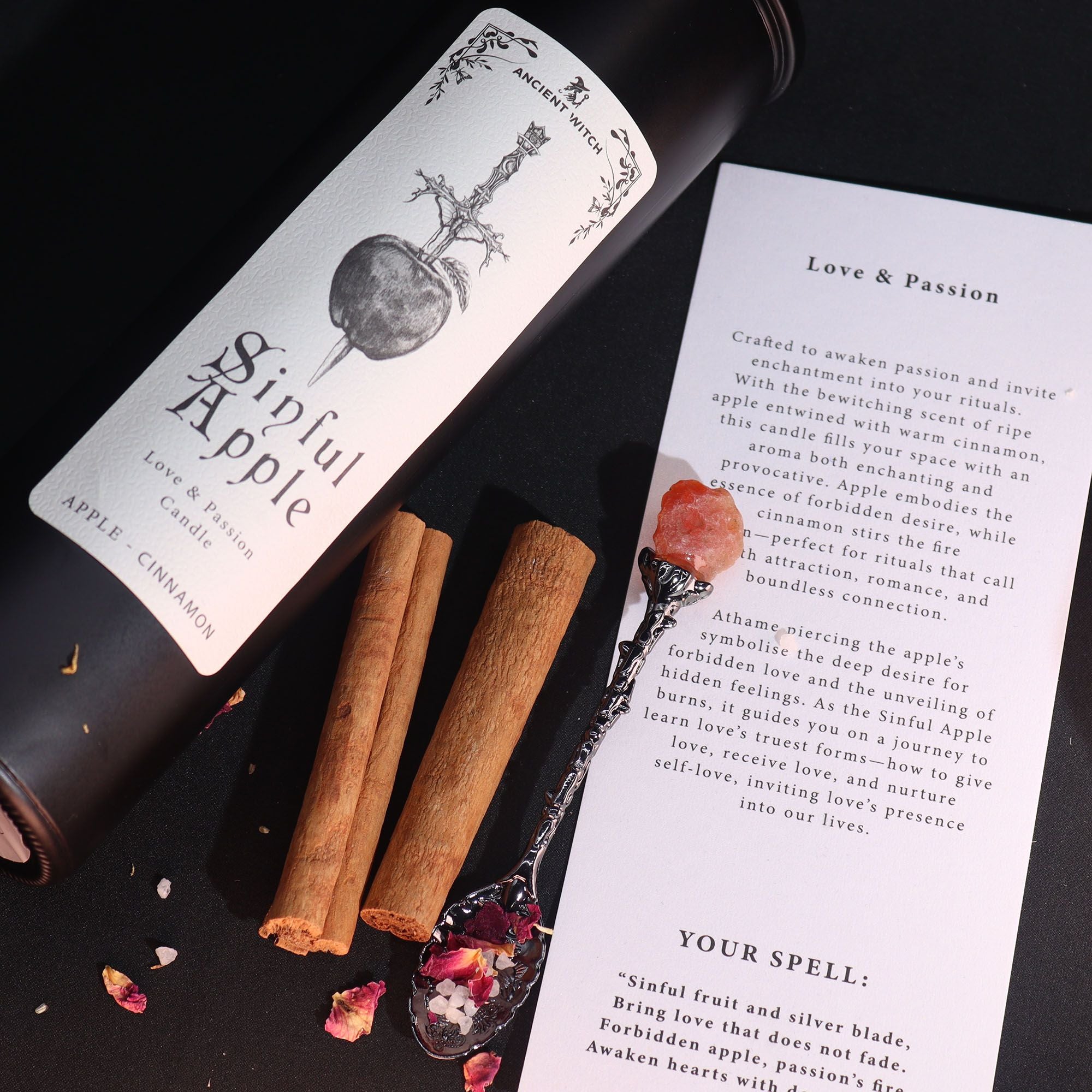 Candle labeled 'Sinful Apple' with cinnamon sticks and a decorative spoon on a dark surface.