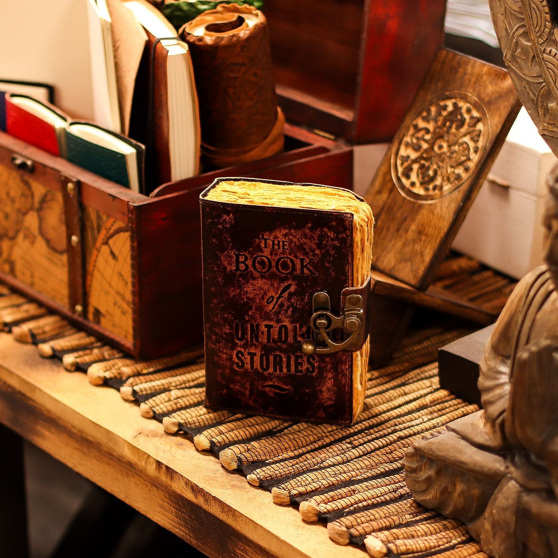 Decorative book with ornate cover on a wooden surface with books and a statue in the background