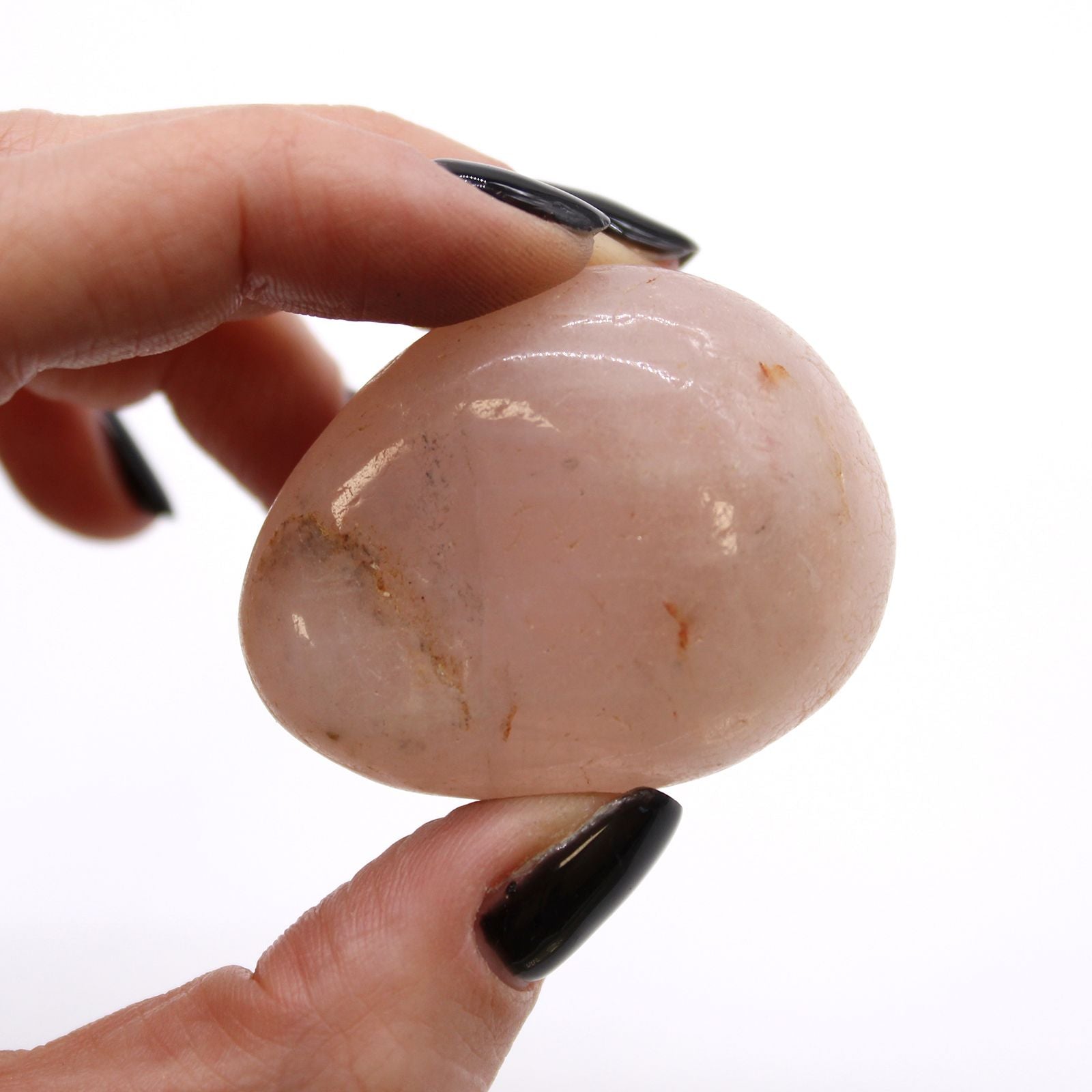 Hand holding a smooth, pinkish stone against a white background