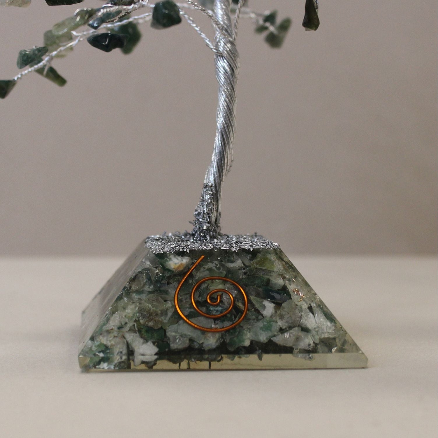 Decorative piece with a tree on a pyramid base featuring green stones and a copper coil.