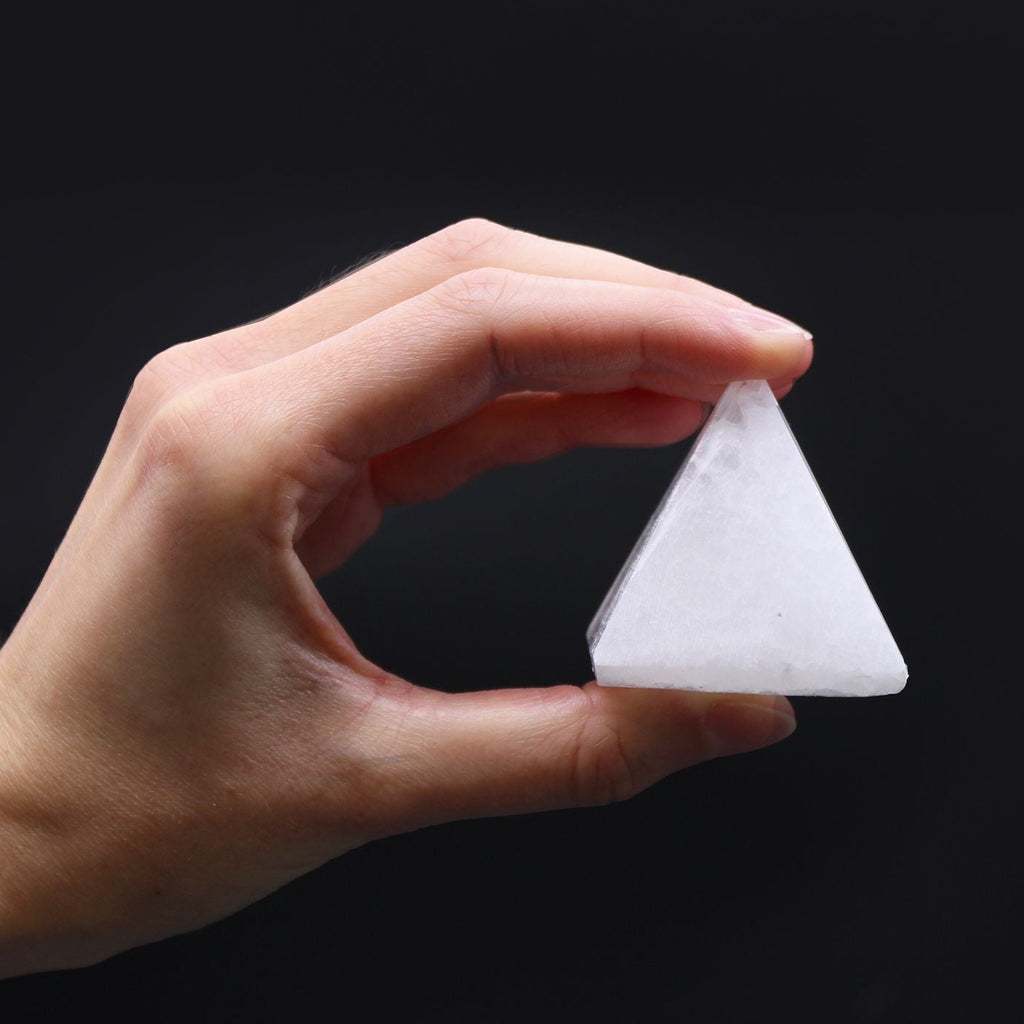 Hand holding a triangular white stone against a black background