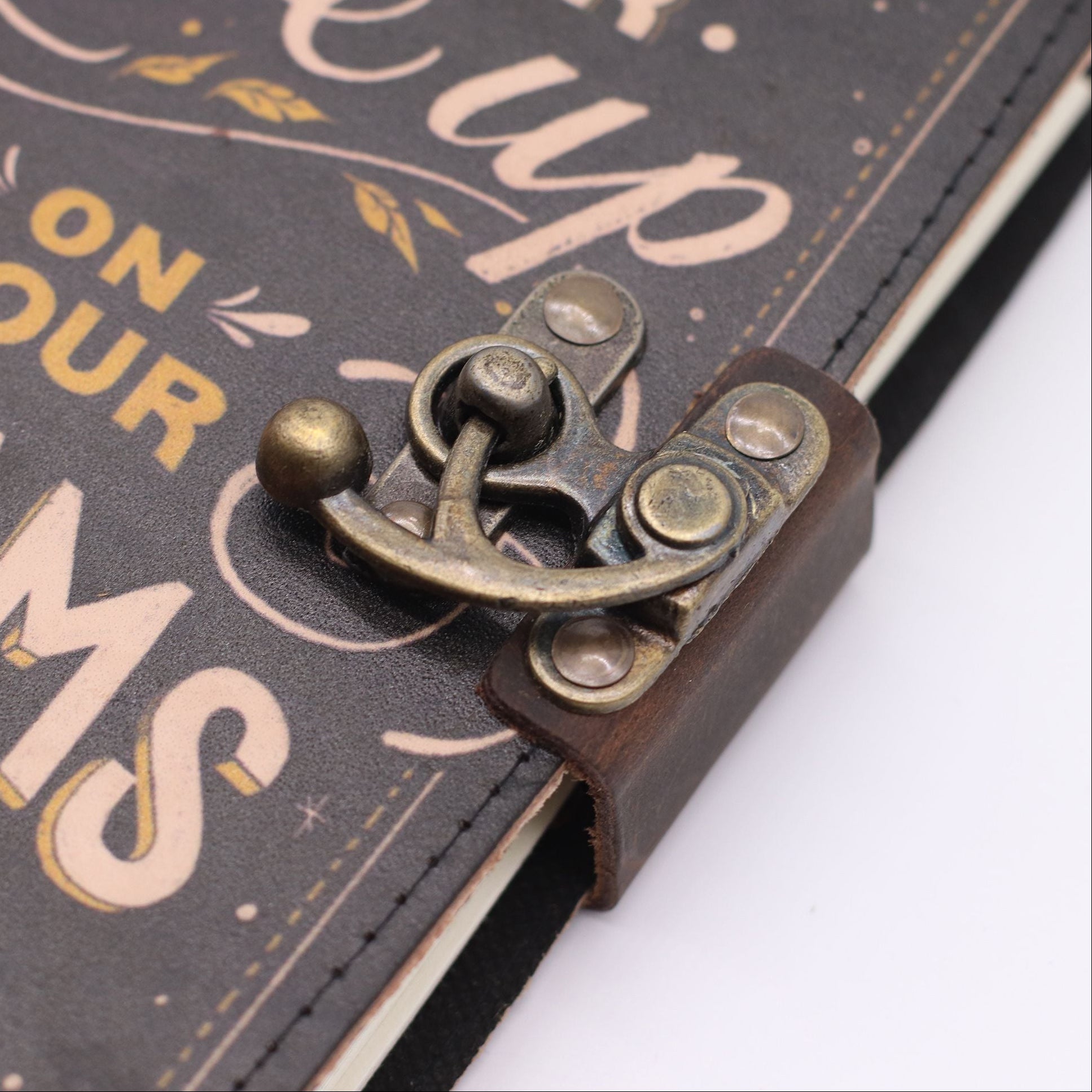 Close-up of a decorative latch on a leather-bound book with text in the background.