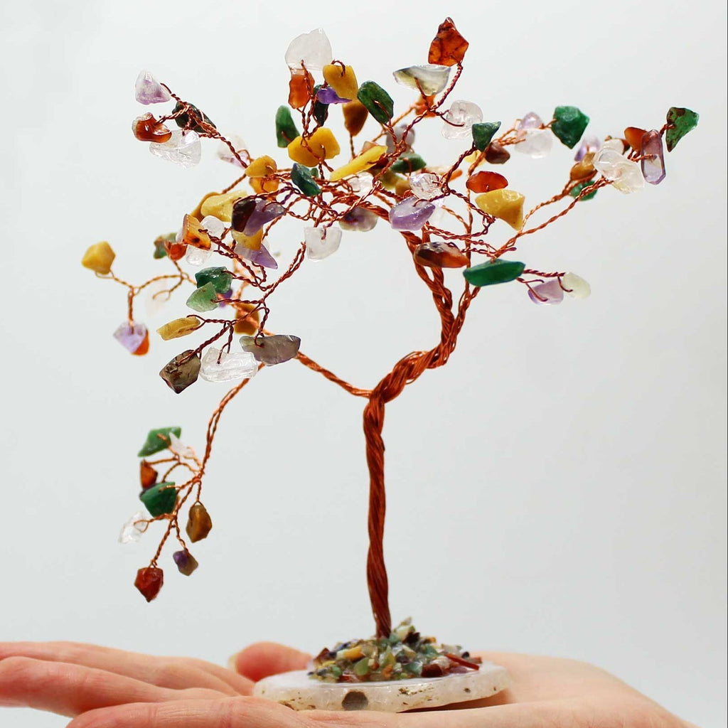 Hand holding a small tree made of multicolored stones against a white background