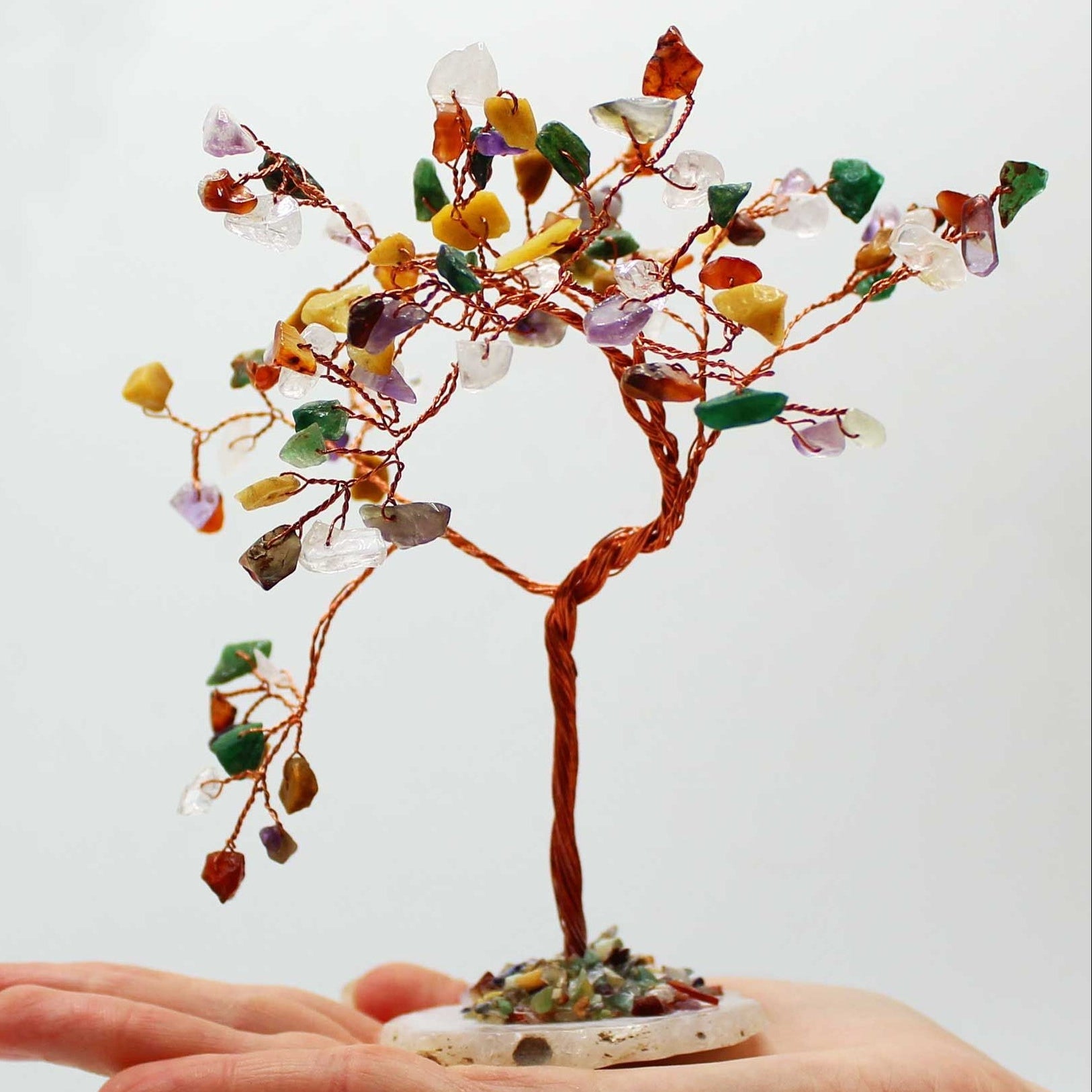 Hand holding a small tree made of multicolored stones against a white background
