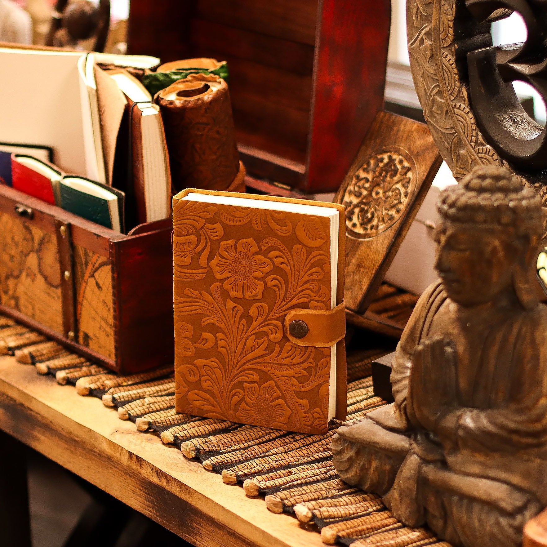 Decorative wooden notebook with intricate designs on a wooden surface with a Buddha statue.