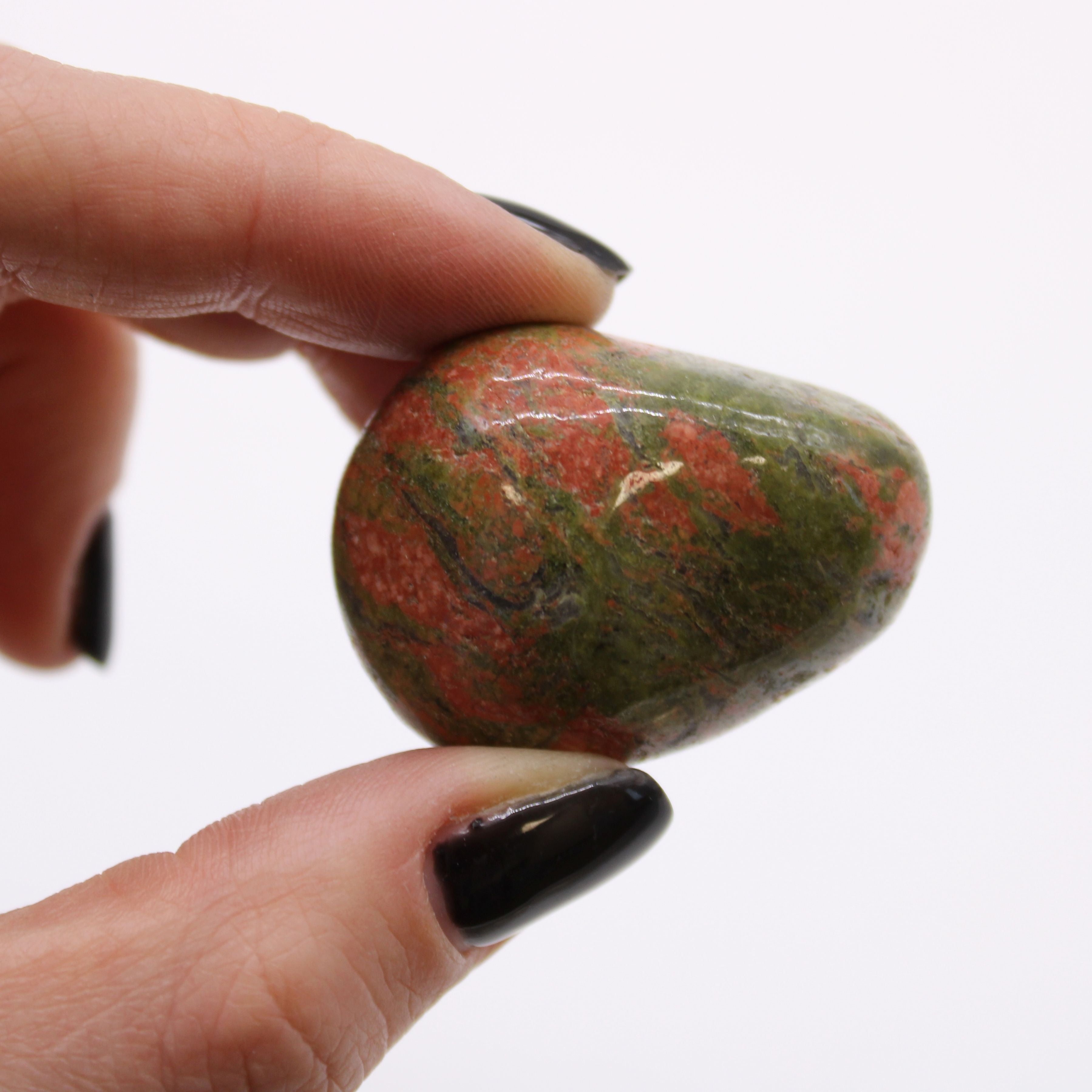 Hand holding a marbled stone with red and green colors against a white background