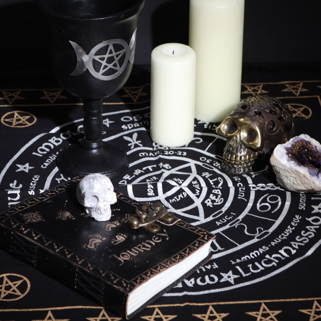 Witchcraft setup with black goblet, candles, skull, and crystal on a black book with white text.