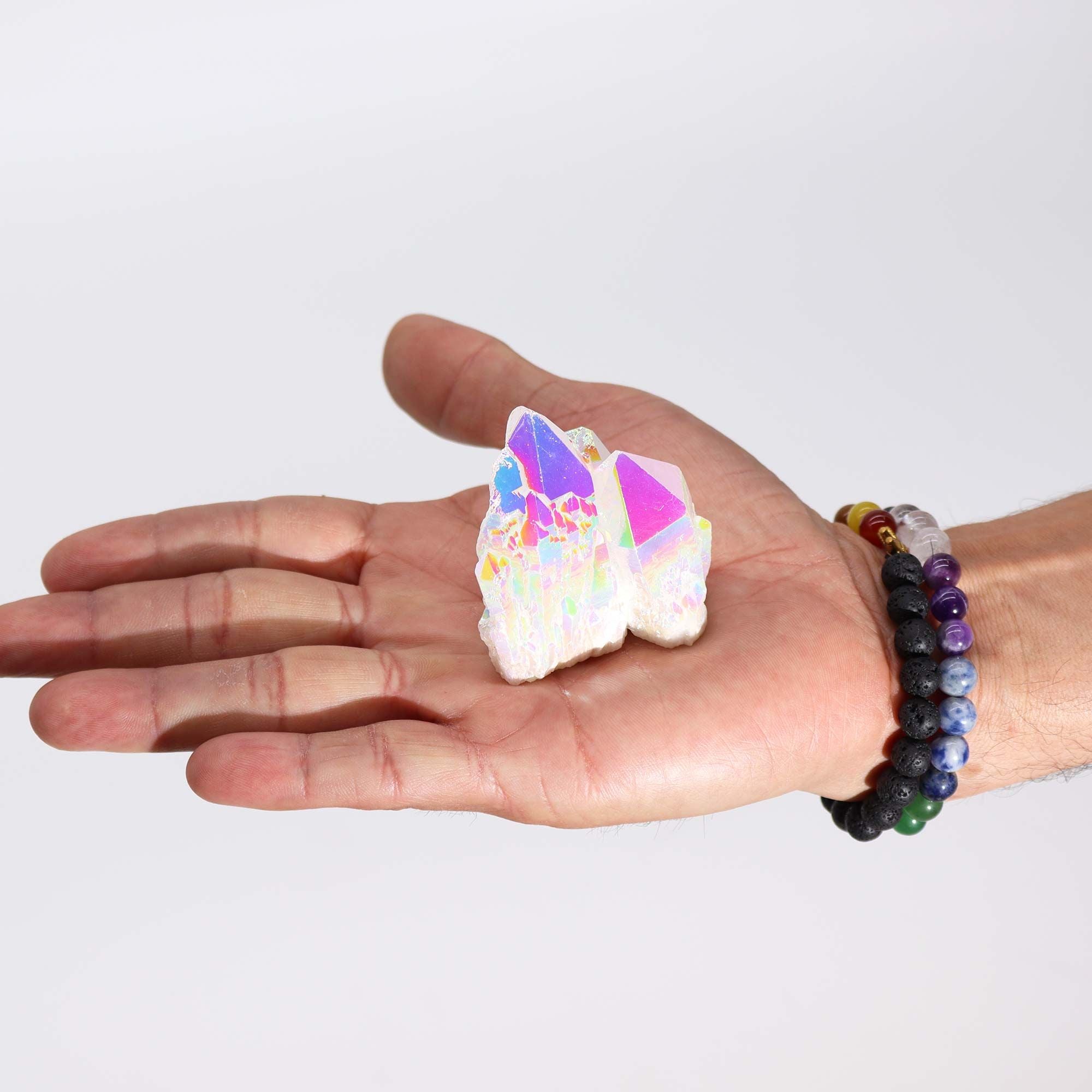 Hand holding a colorful crystal with a multicolored beaded bracelet on a plain background