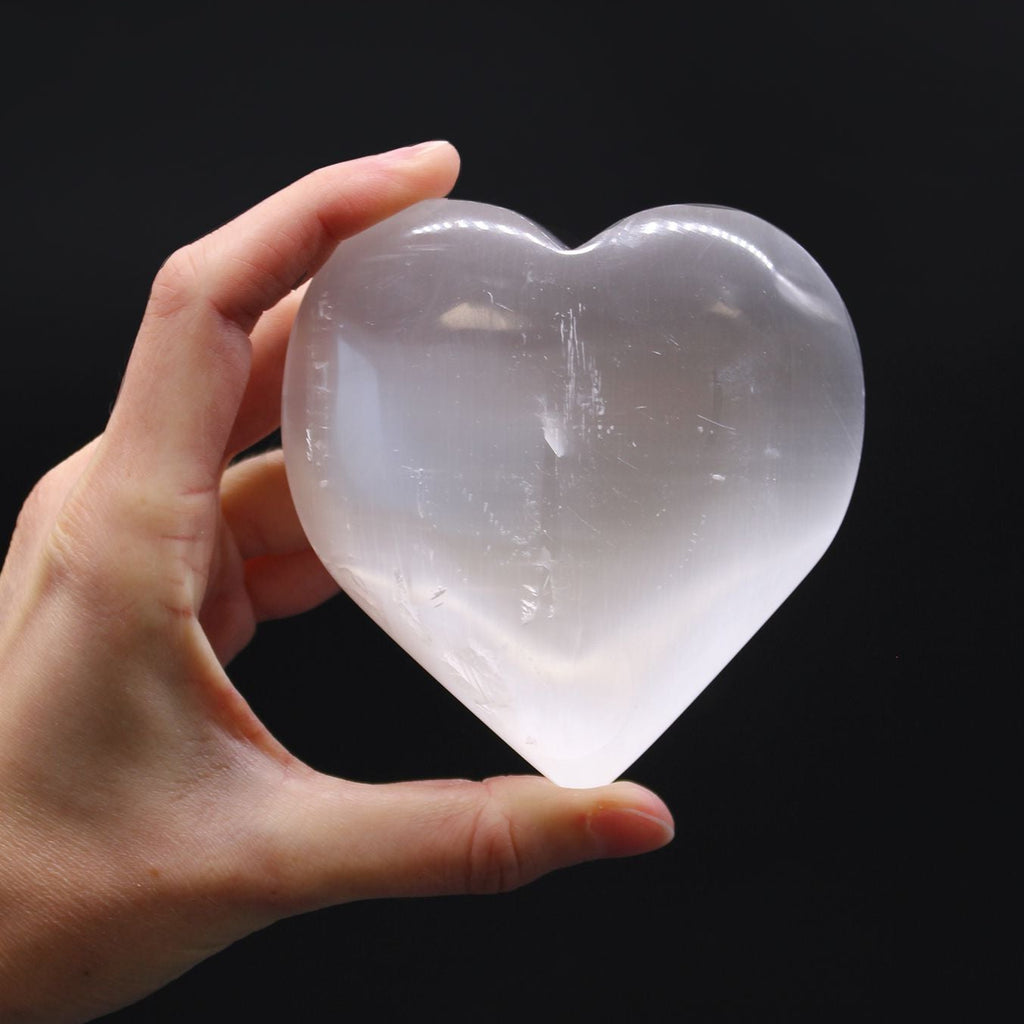Hand holding a clear crystal heart against a black background