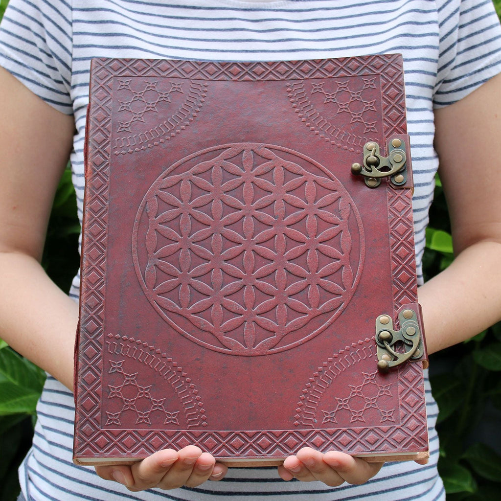 Person holding a red leather notebook with embossed design and metal clasp against a green leafy background