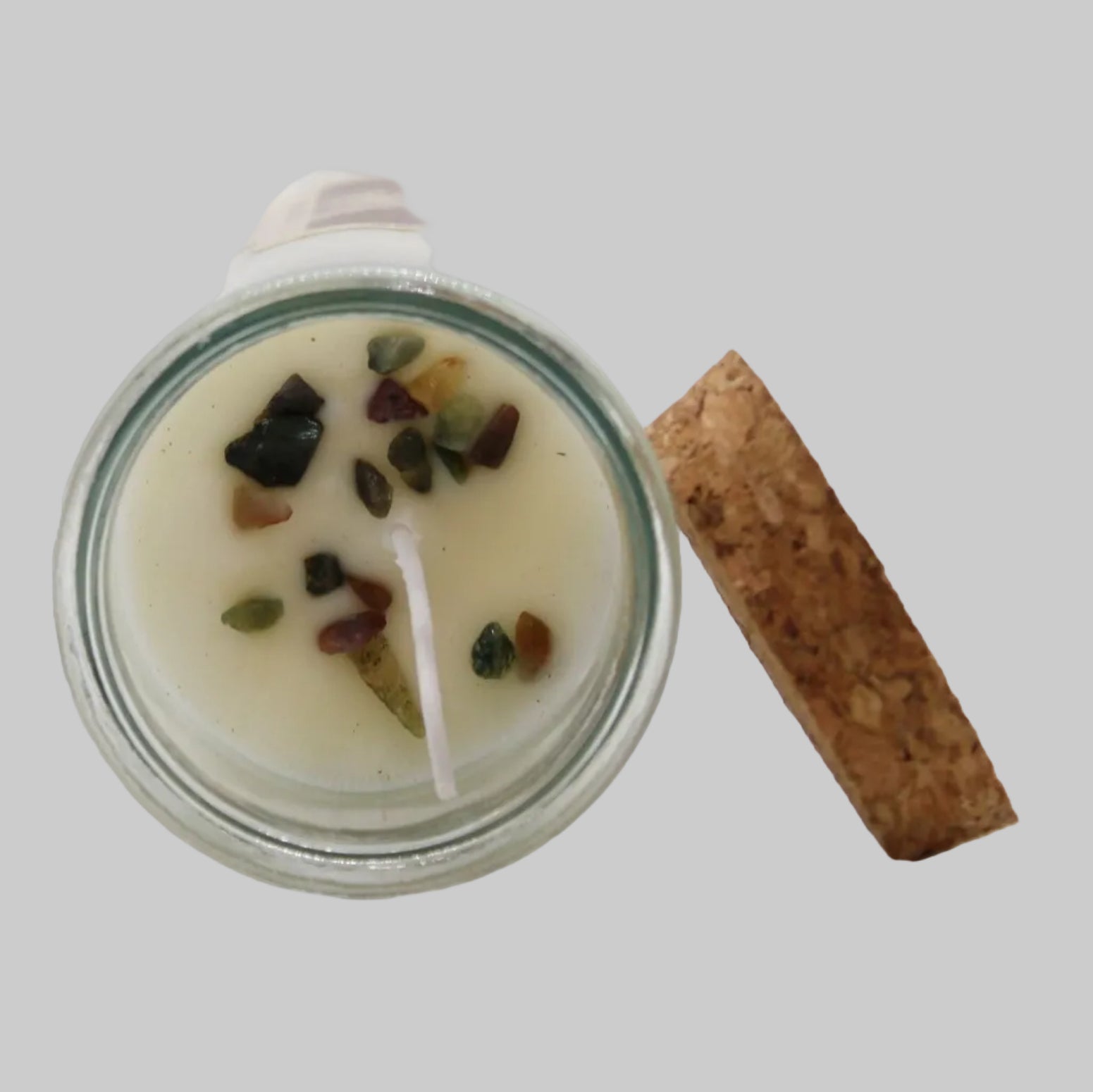 Candle in a glass jar with decorative stones and a cork lid on a white background