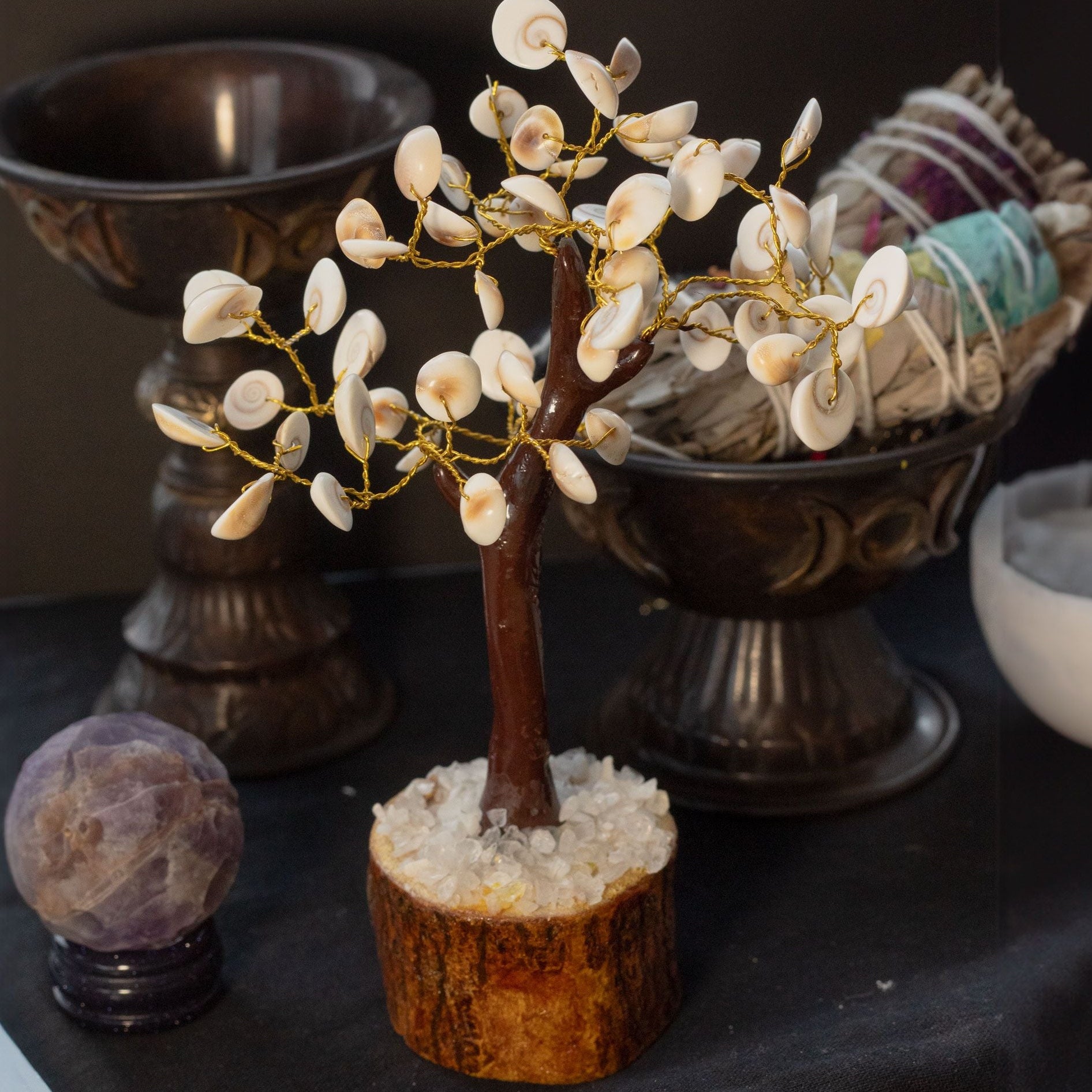 Decorative tree with white flowers on a dark surface with other decorative items.