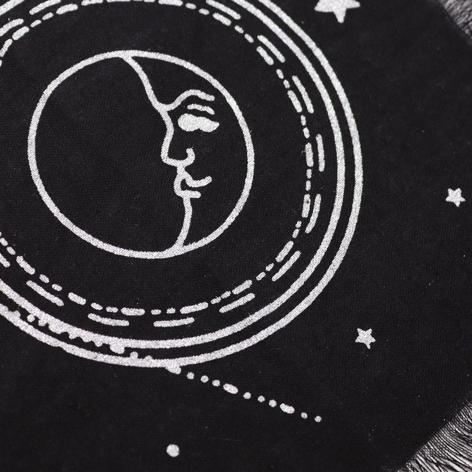 Black fabric with white embroidered design of a face within a circular pattern and stars.