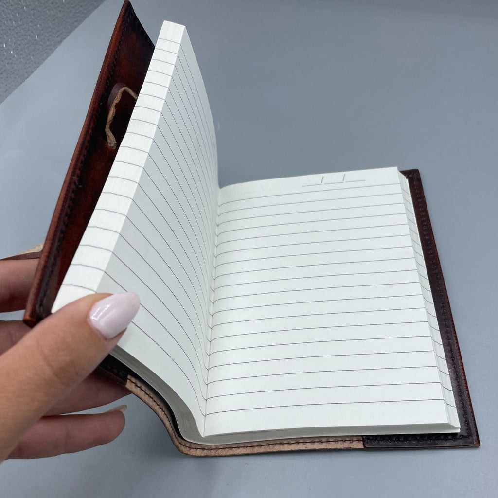 Hand holding an open notebook with lined pages against a gray background