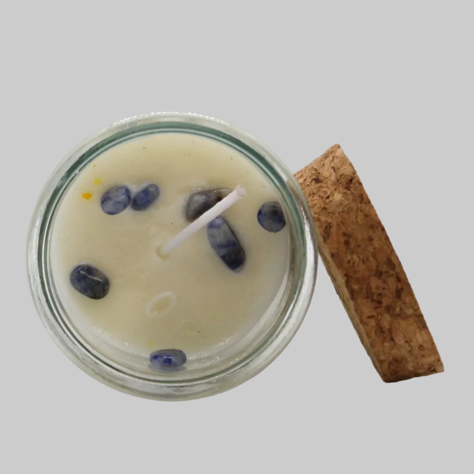 Candle in a glass jar with decorative stones and a cork lid on a white background