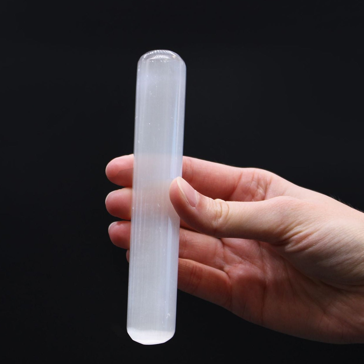 Hand holding a clear crystal rod against a black background
