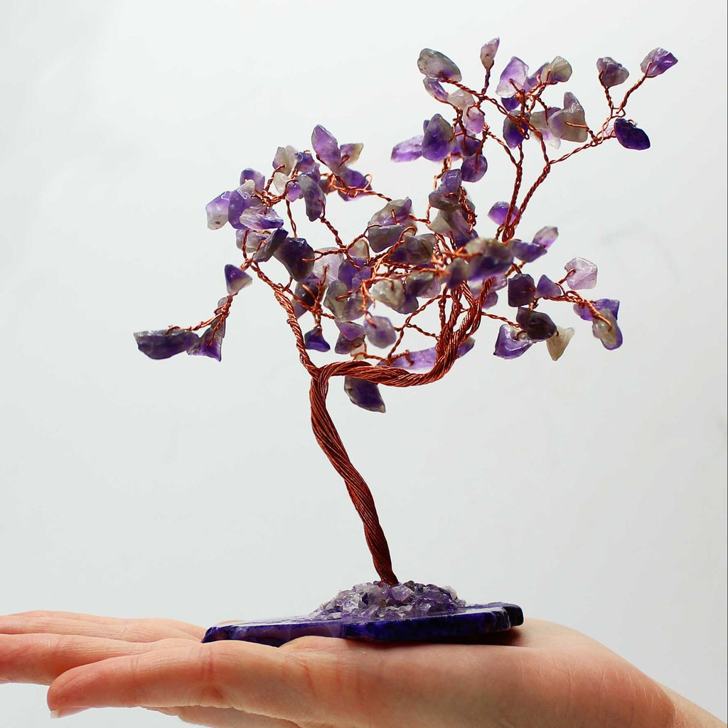 Hand holding a small tree sculpture with purple and brown elements on a white background