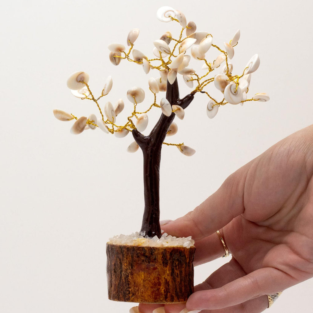 Hand holding a small decorative tree with white flowers on a light background