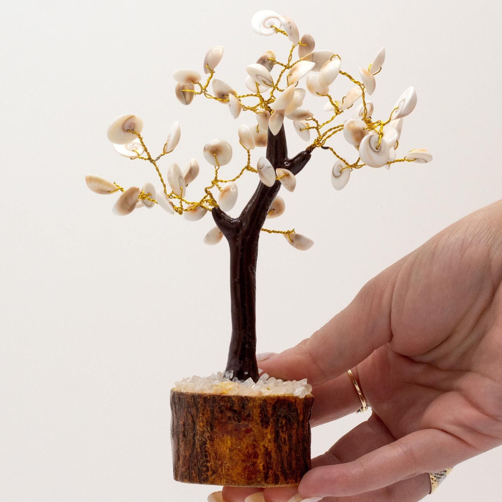 Hand holding a small decorative tree with white flowers on a light background