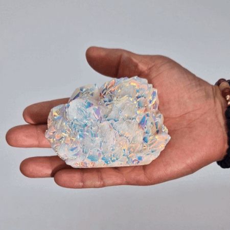 Hand holding a large crystal with iridescent properties against a plain background