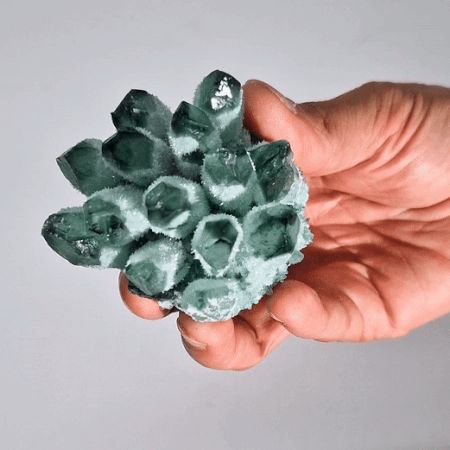 Hand holding a green crystal against a gray background
