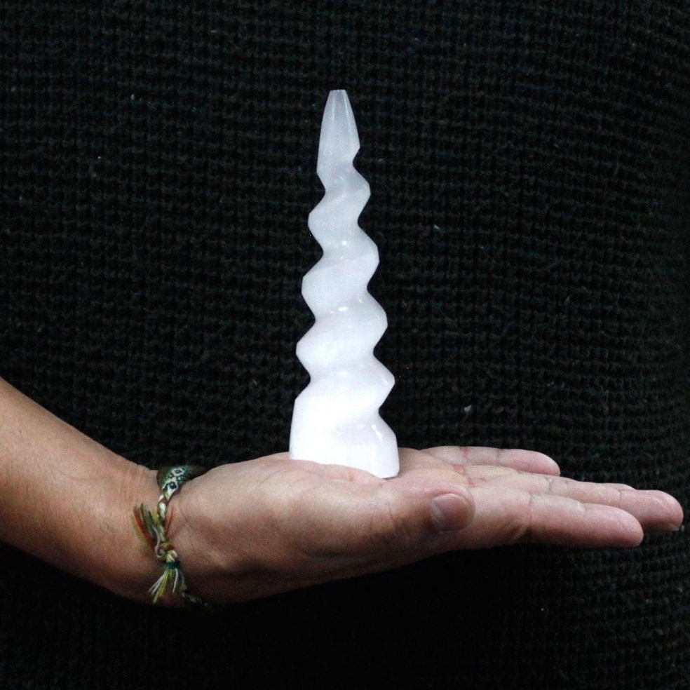 Person holding a spiral ice sculpture in their palm against a black background