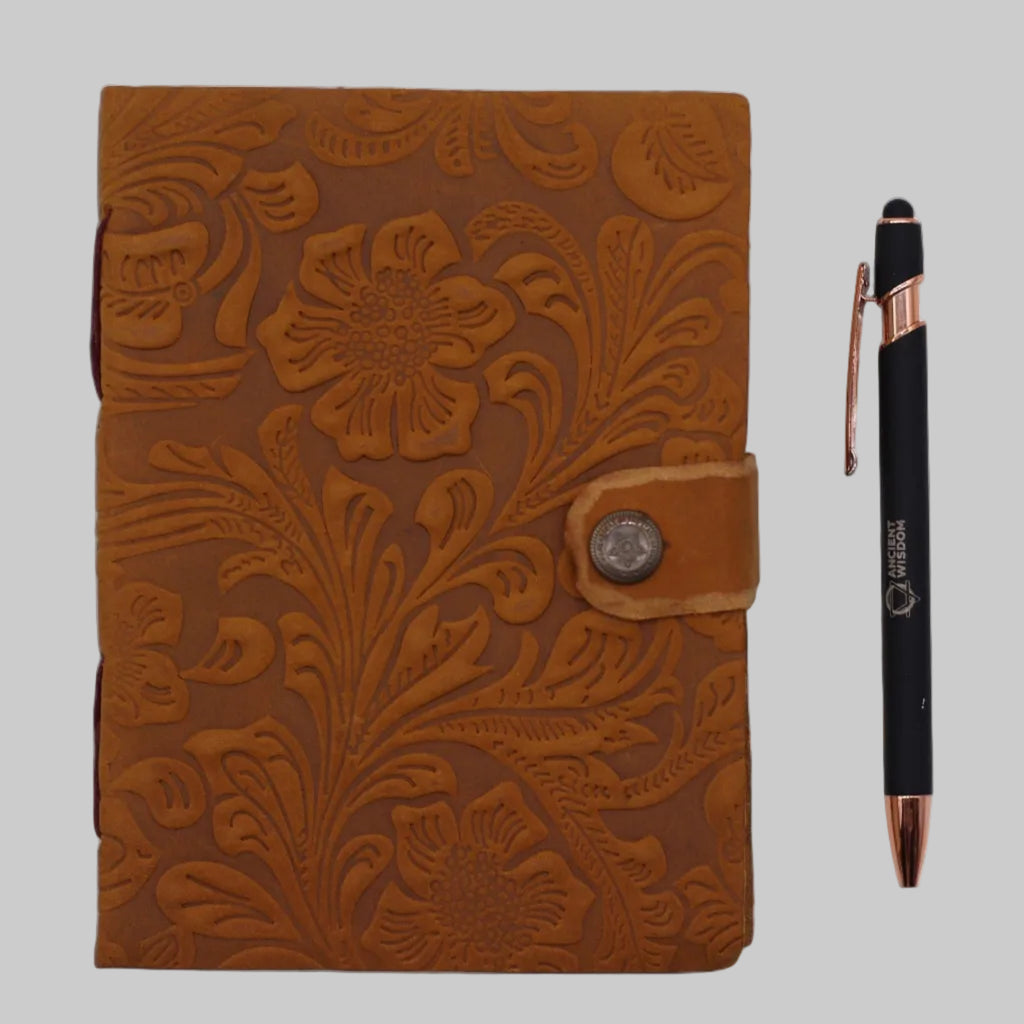 Brown floral embossed leather notebook with a pen on a white background