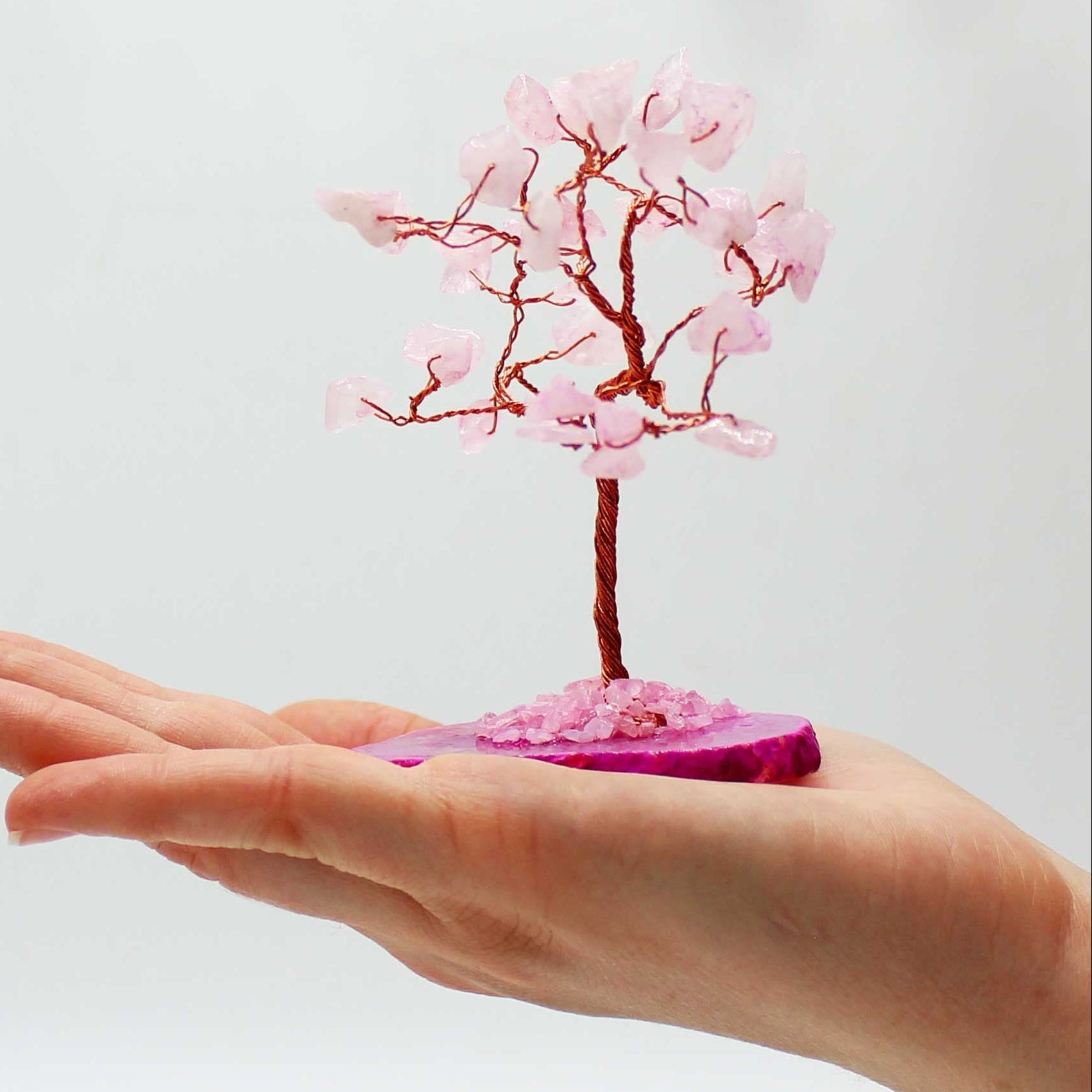 Small pink tree on a pink base held in a hand against a light gray background