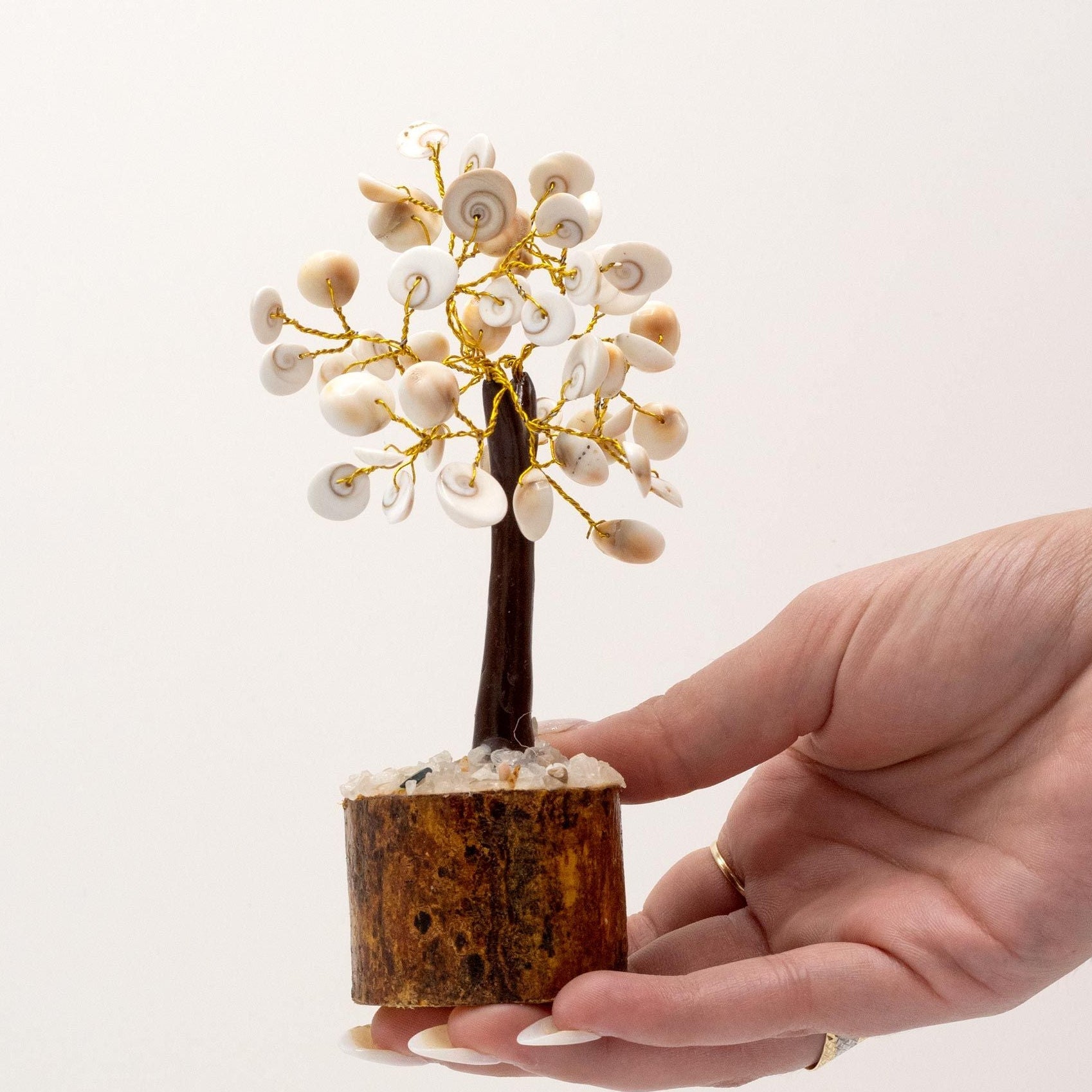 Hand holding a small decorative tree with white flowers and gold accents on a plain background