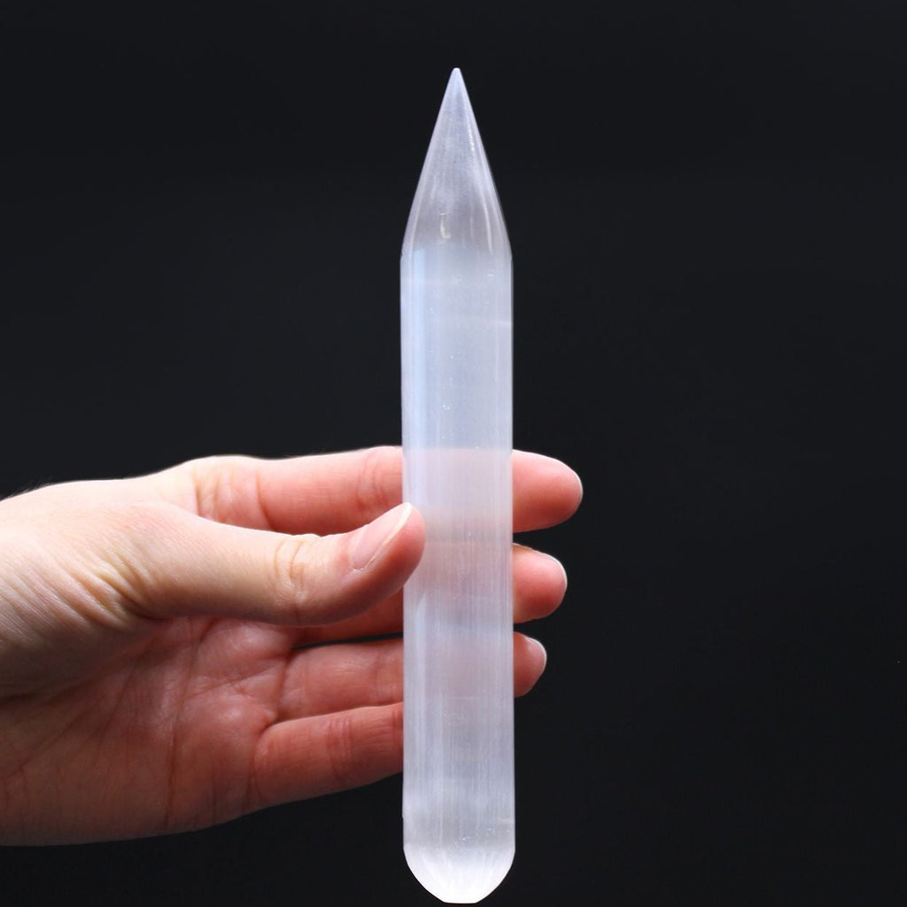 Hand holding a clear crystal point against a black background