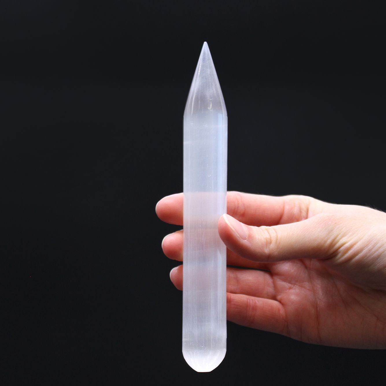 Hand holding a clear crystal point against a black background