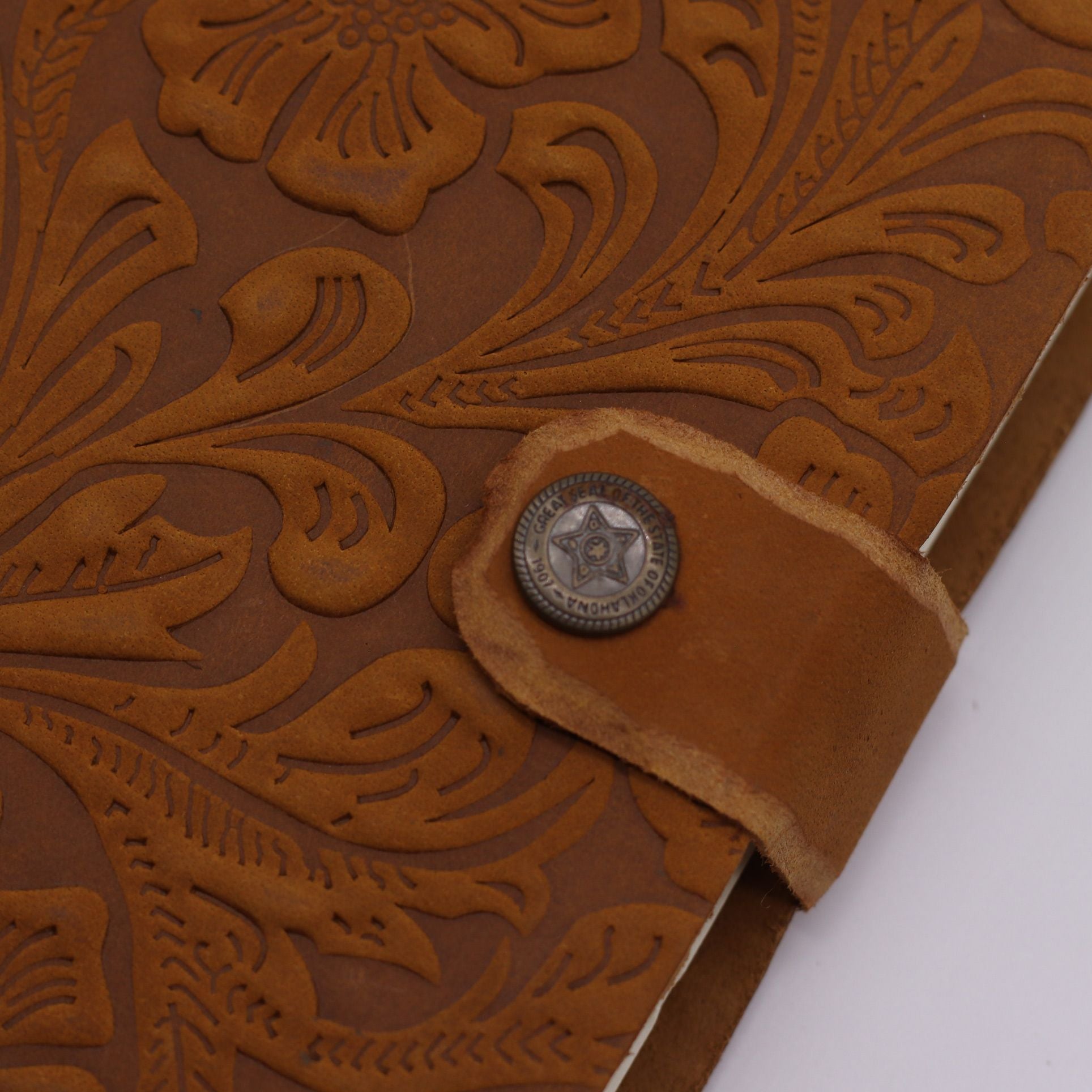 Close-up of a brown leather wallet with intricate embossed design and a metal button on a white background