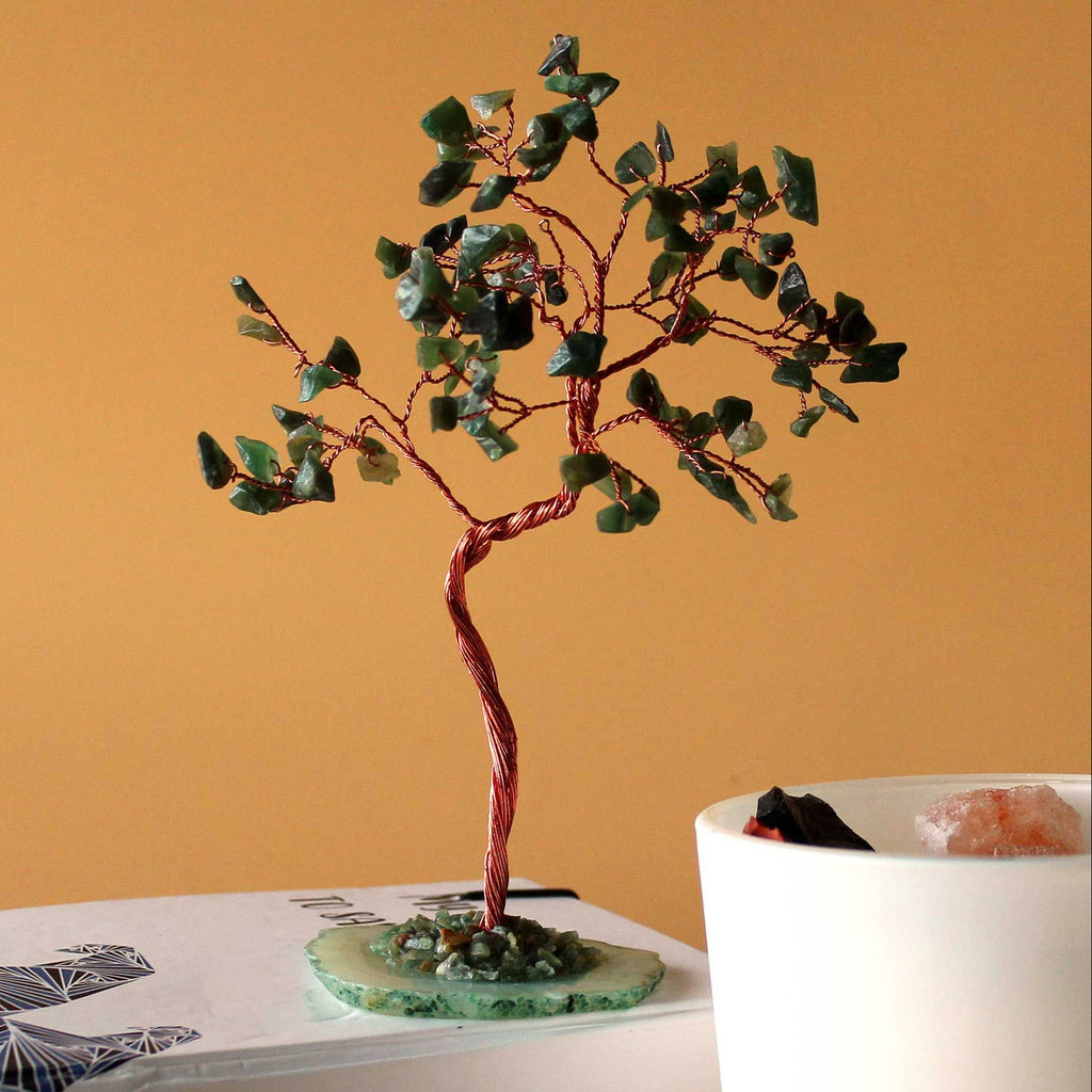 Decorative tree with green leaves on a white base against an orange wall