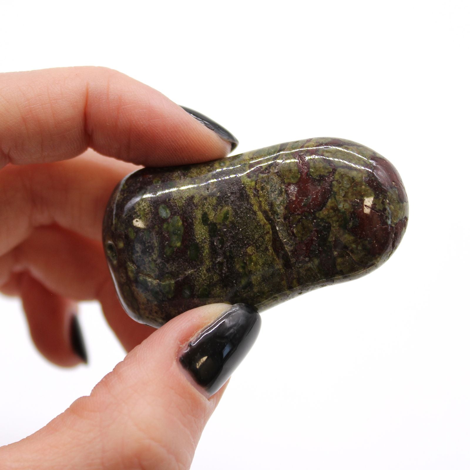 Hand holding a polished stone with a green and brown pattern against a white background