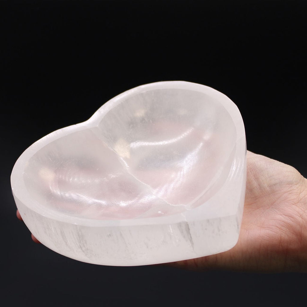 Heart-shaped crystal held in a hand against a black background